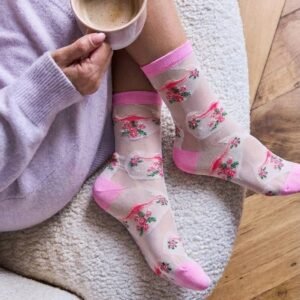 Top view Picture of woman relaxing holding a cup of coffee wearing a lavender sweater dress and moona uterus novelty socks on a cozy cream chair.